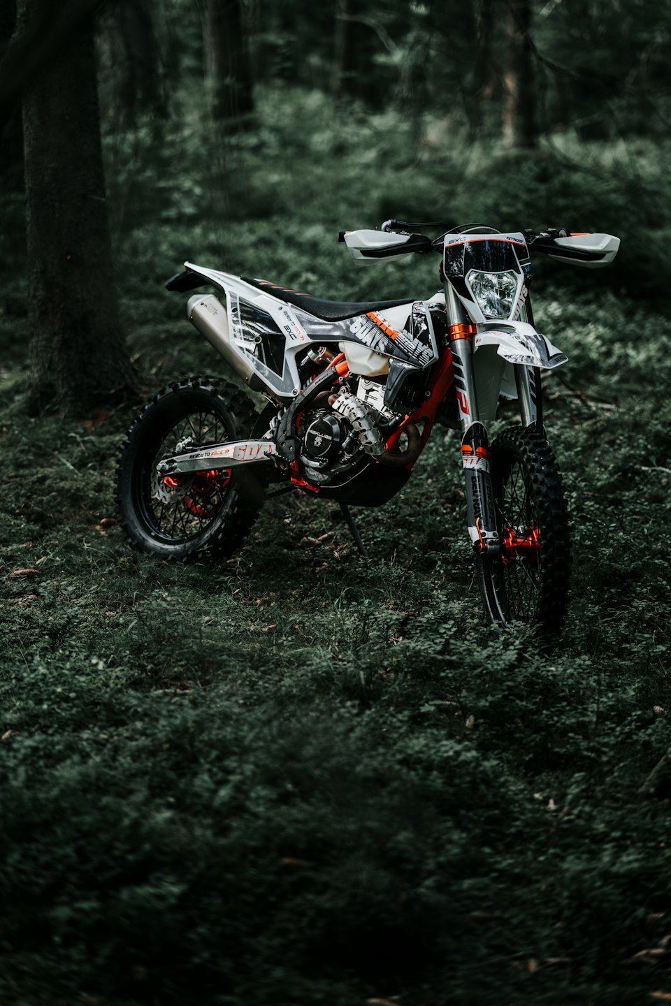 Ein weiß-oranges Enduro-Motorrad steht in einem Wald.